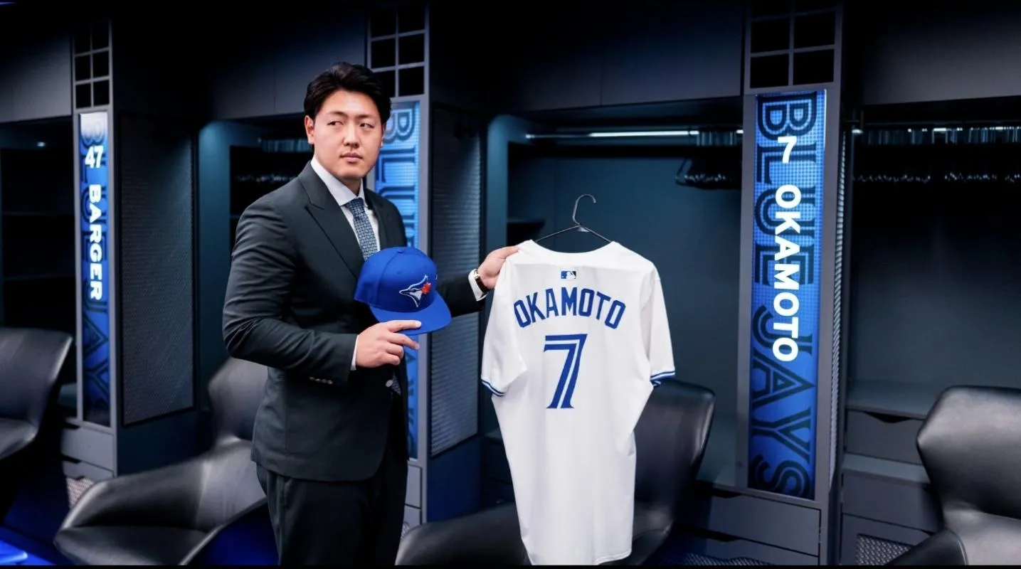 Toronto Blue Jays Kazuma Okamoto (7) holding up his cap and number 7 jersey in the clubhouse at Rogers Centre.