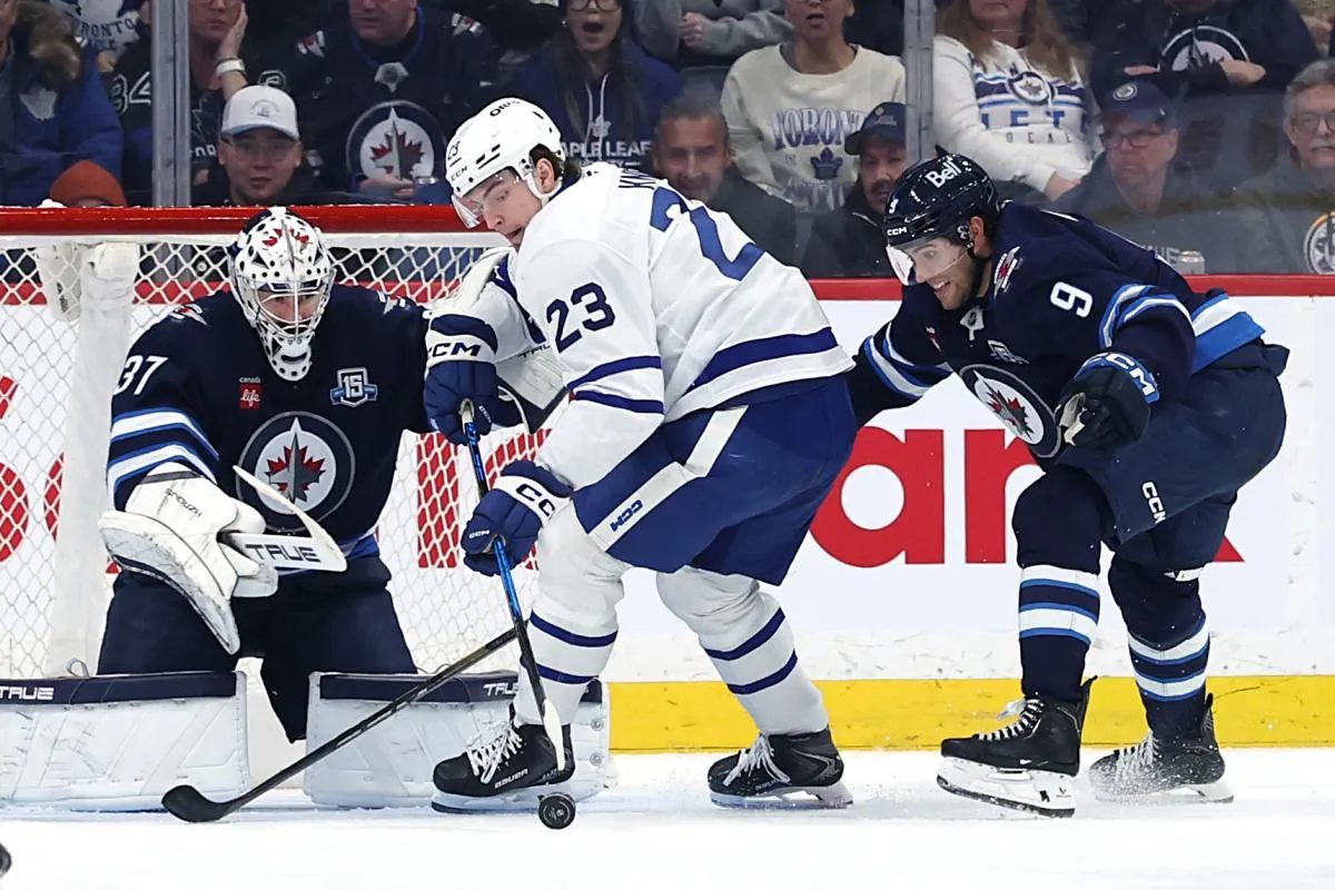 Toronto Maple Leafs left wing Matthew Knies (23) is checked by Winnipeg Jets left wing Alex Iafallo (9) in front of Winnipeg Jets goaltender Connor Hellebuyck (37) in the second period at Canada Life Centre.