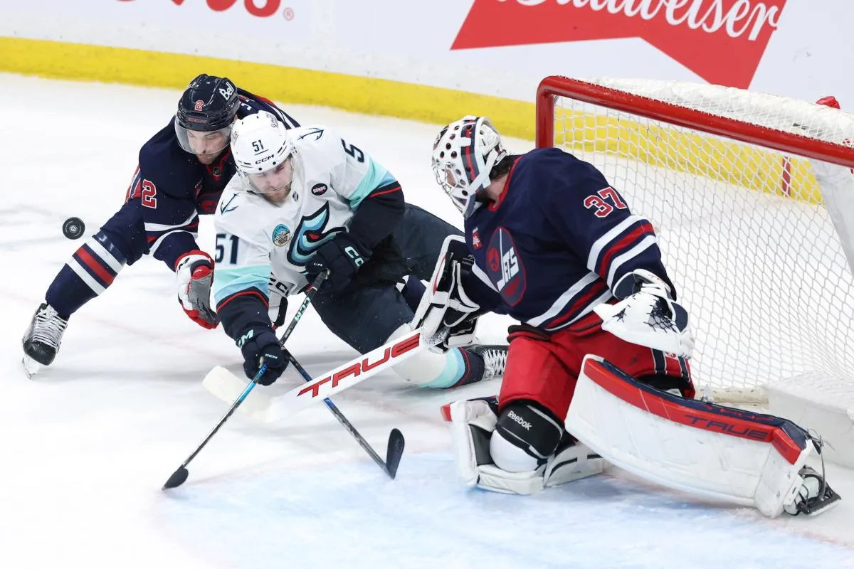 Seattle Kraken center Shane Wright (51) is taken down by Winnipeg Jets defenseman Dylan DeMelo (2), attempting a shot on Winnipeg Jets goaltender Connor Hellebuyck (37) in the third period at Canada Life Centre.