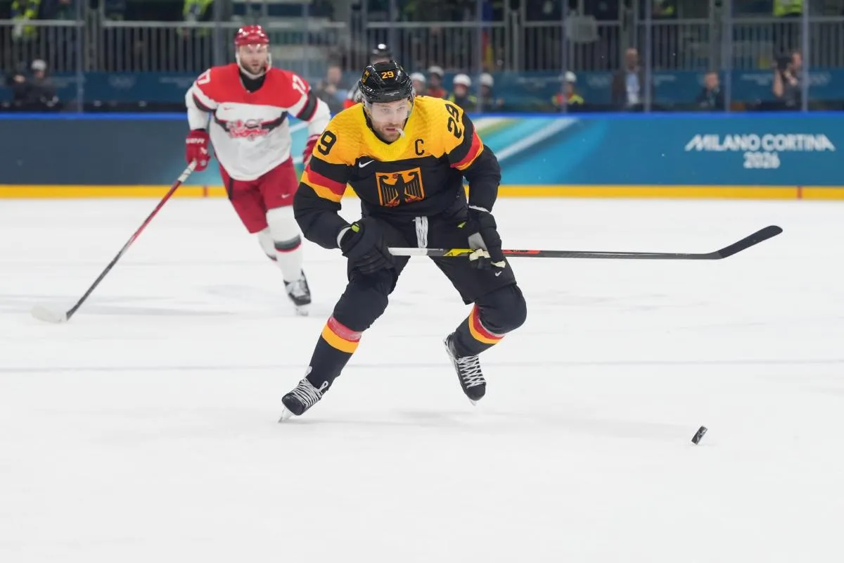Leon Draisaitl of Germany skates with the puck past Oliver Lauridsen of Denmark and Phillip Bruggisser of Denmark in men's ice hockey Group C play during the Milano Cortina 2026 Olympic Winter Games at Milano Rho Ice Hockey Arena.
