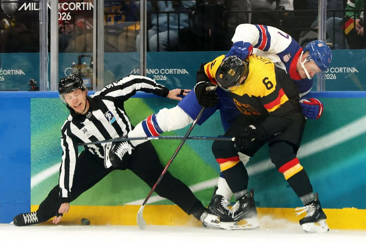 Brady Tkachuk of United States in action with Kai Wissmann of Germany as linesperson Nick Briganti looks on in men's ice hockey group C play during the Milano Cortina 2026 Olympic Winter Games at Milano Santagiulia Ice Hockey Arena.