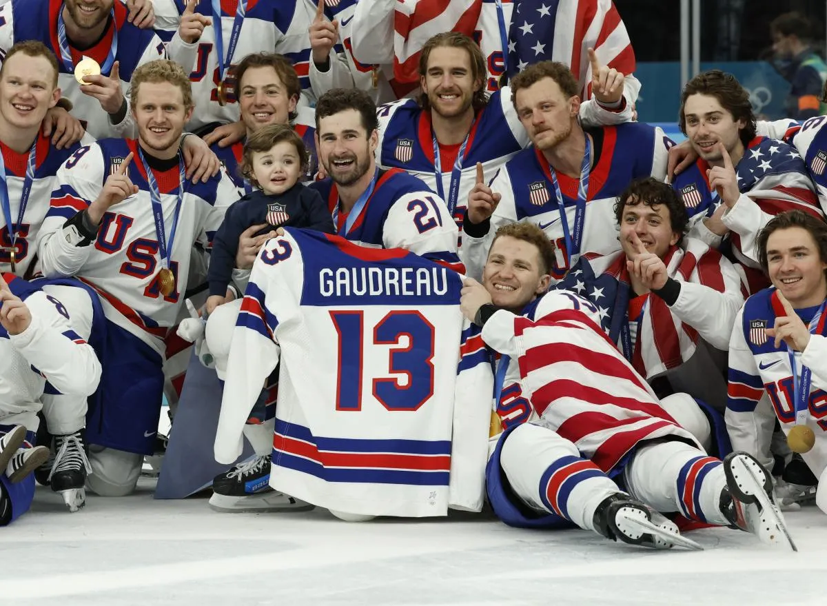 United States players celebrate with a team photo while holding the jersey of Johnny Gaudreau after defeating Canada in the men's ice hockey gold medal game during the Milano Cortina 2026 Olympic Winter Games at Milano Santagiulia Ice Hockey Arena.
