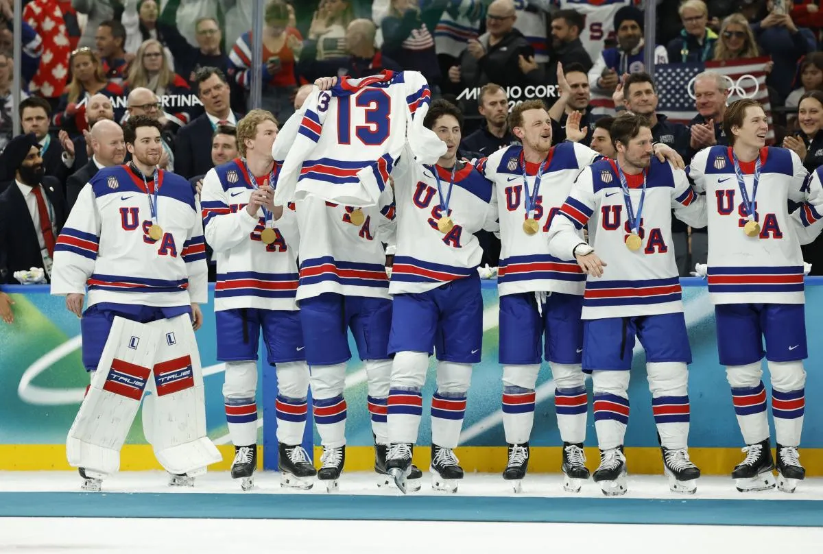 United States players celebrate with their gold medals and the jersey of Johnny Gaudreau after defeating Canada in the men's ice hockey gold medal game during the Milano Cortina 2026 Olympic Winter Games at Milano Santagiulia Ice Hockey Arena.