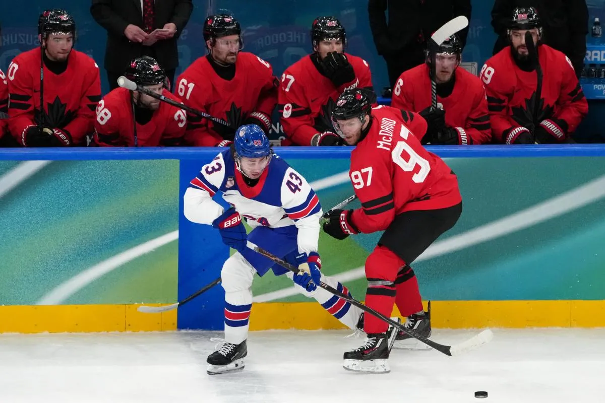 Quinn Hughes of the United States battles for the puck against Connor McDavid of Canada during the men's ice hockey gold medal game during the Milano Cortina 2026 Olympic Winter Games at Milano Santagiulia Ice Hockey Arena.