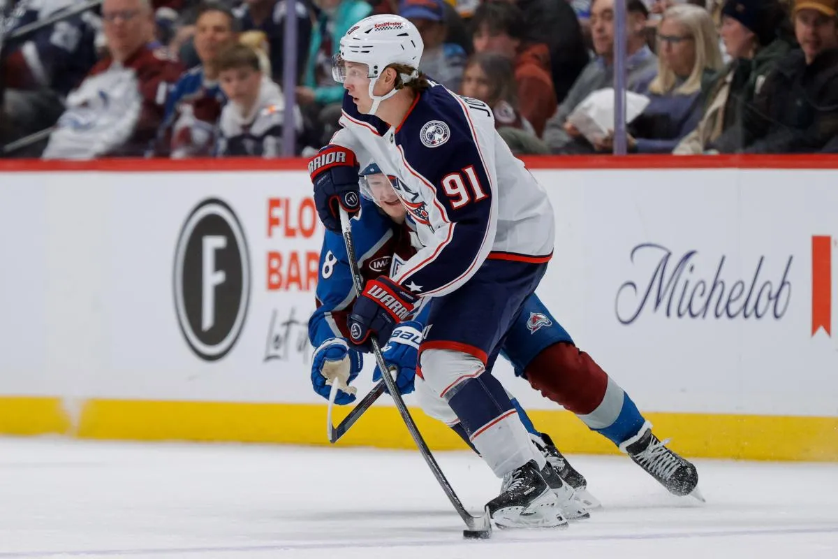 Columbus Blue Jackets center Kent Johnson (91) controls the puck under pressure from Colorado Avalanche defenseman Cale Makar (8) in the second period at Ball Arena