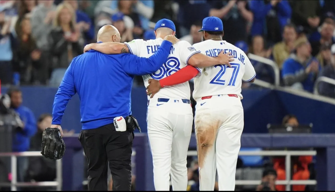 March 28, 2026: Toronto Blue Jays head trainer Jose Minestral, and first baseman Vladimir Guerrero Jr help left-handed pitcher Mason Fluharty off the field at Rogers Center