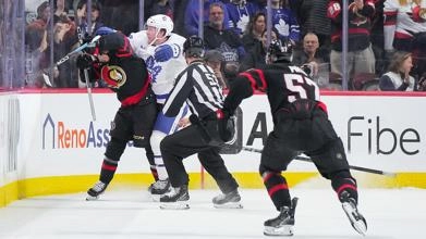 Morgan Rielly of the Toronto Maple Leafs cross-checking Ridly Greig of the Ottawa Senators.