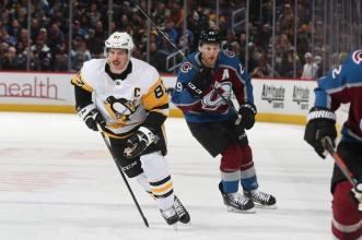 Pittsburgh Penguins captain and forward Sidney Crosby skating up ice next to Colorado Avalanche forward Nathan MacKinnon during an away game in the NHL.