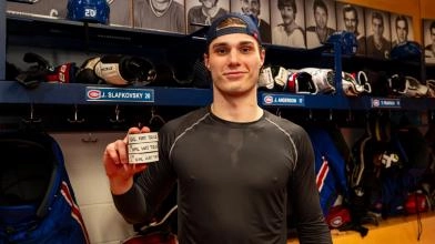 Juraj Slafkovsky in the Montreal Canadiens' locker room, holding three pucks after scoring a hat trick against the Philadelphia Flyers.
