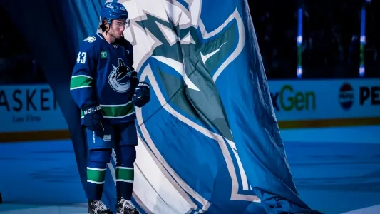 Vancouver Canucks' Quinn Hughes stands next to a team flag
