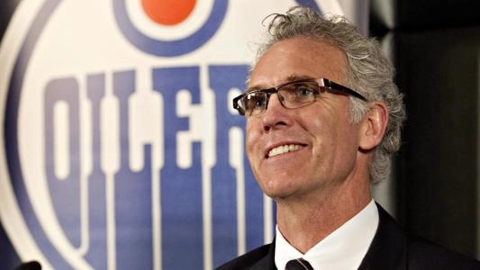 Craig MacTavish smiles in front of an Edmonton Oilers logo