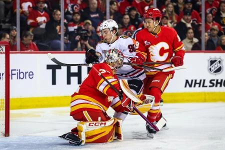 7 novembre 2025; Calgary, Alberta, Canada; Le d&eacute;fenseur des Flames de Calgary, Zayne Parekh (19), et le centre des Blackhawks de Chicago, Connor Bedard (98), se disputent la rondelle devant le gardien des Flames de Calgary, Dustin Wolf (32), durant la premi&egrave;re p&eacute;riode au Scotiabank Saddledome.