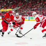 Mar 14, 2025; Raleigh, North Carolina, USA; Carolina Hurricanes left wing Eric Robinson (50) skates with the puck against Detroit Red Wings right wing Dominik Shine (50) and defenseman Simon Edvinsson (77) during the first period at Lenovo Center. Mandatory Credit: James Guillory-Imagn Images