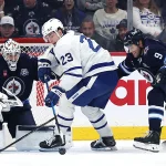 Jan 17, 2026; Winnipeg, Manitoba, CAN; Toronto Maple Leafs left wing Matthew Knies (23) is checked by Winnipeg Jets left wing Alex Iafallo (9) in front of Winnipeg Jets goaltender Connor Hellebuyck (37) in the second period at Canada Life Centre.