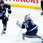 Apr 16, 2024; Winnipeg, Manitoba, CAN; Winnipeg Jets goalie Connor Hellebuyck (37) makes a save against the Seattle Kraken as Winnipeg Jets forward Mark Scheifele (55) looks for a rebound during the third period at Canada Life Centre.