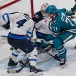 Nov 7, 2025; San Jose, California, USA; San Jose Sharks center Macklin Celebrini (71) shoots the puck in the goal crease against Winnipeg Jets goaltender Connor Hellebuyck (37) and defenseman Neal Pionk (4) during the third period at SAP Center at San Jose. Mandatory Credit: David Gonzales-Imagn Images
