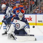 Oct 9, 2024; Edmonton, Alberta, CAN; Winnipeg Jets goaltender Connor Hellebuyck (37) and Edmonton Oilers forward Zach Hyman (18) look for a loose puck during the first period at Rogers Place.