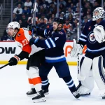 Apr 11, 2026; Winnipeg, Manitoba, CAN; Winnipeg Jets defenseman Neal Pionk (4) jostles for position with Philadelphia Flyers forward Noah Cates (27) in front of Winnipeg Jets goalie Connor Hellebuyck (37) during the first period at Canada Life Centre.