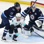 Apr 6, 2026; Winnipeg, Manitoba, CAN; Winnipeg Jets center Adam Lowry (17) checks Seattle Kraken right wing Jordan Eberle (7) in front of Winnipeg Jets goaltender Connor Hellebuyck (37) in the first period at Canada Life Centre.