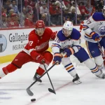 Oct 27, 2024; Detroit, Michigan, USA; Detroit Red Wings defenseman Simon Edvinsson (77) fights for control of the puck against Edmonton Oilers left wing Zach Hyman (18) during the third period at Little Caesars Arena.