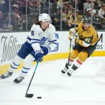 Oct 8, 2026; Las Vegas, Nevada, USA; Toronto Maple Leafs defenseman Chris Tanev (8) skates with the puck against Vegas Golden Knights center Brett Howden (21) in the first period at T-Mobile Arena.